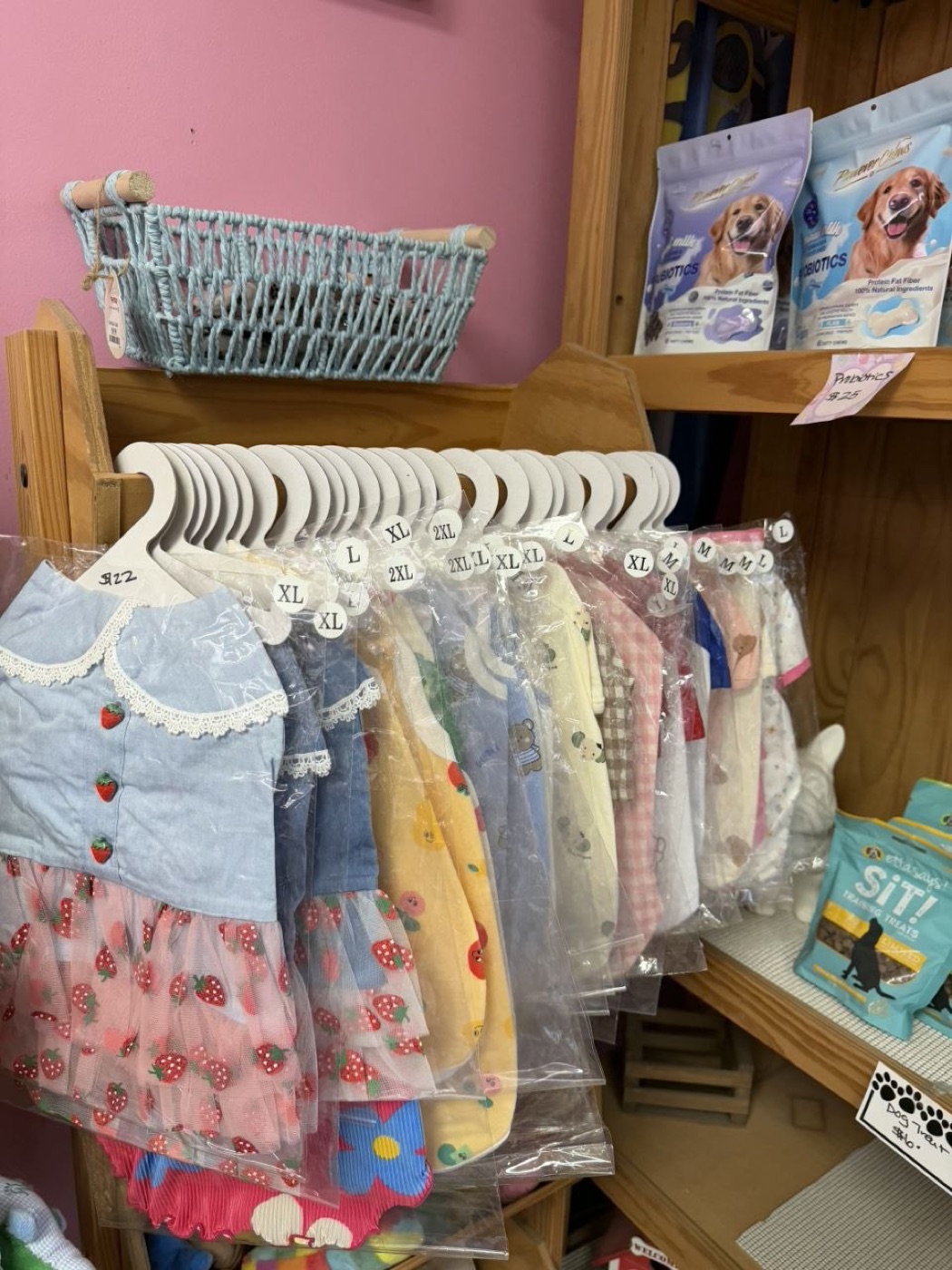 A rack of dog dresses and shirts on hangers marked with sizes, next to the probiotic chews